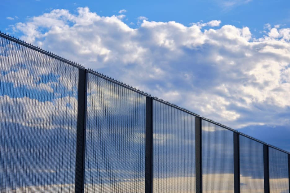 Tall black metal security fencing against a blue sky